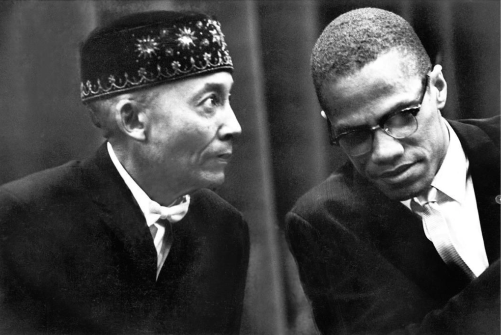 A b&w shot of Elijah Muhammad and Malcolm X in conversation. 